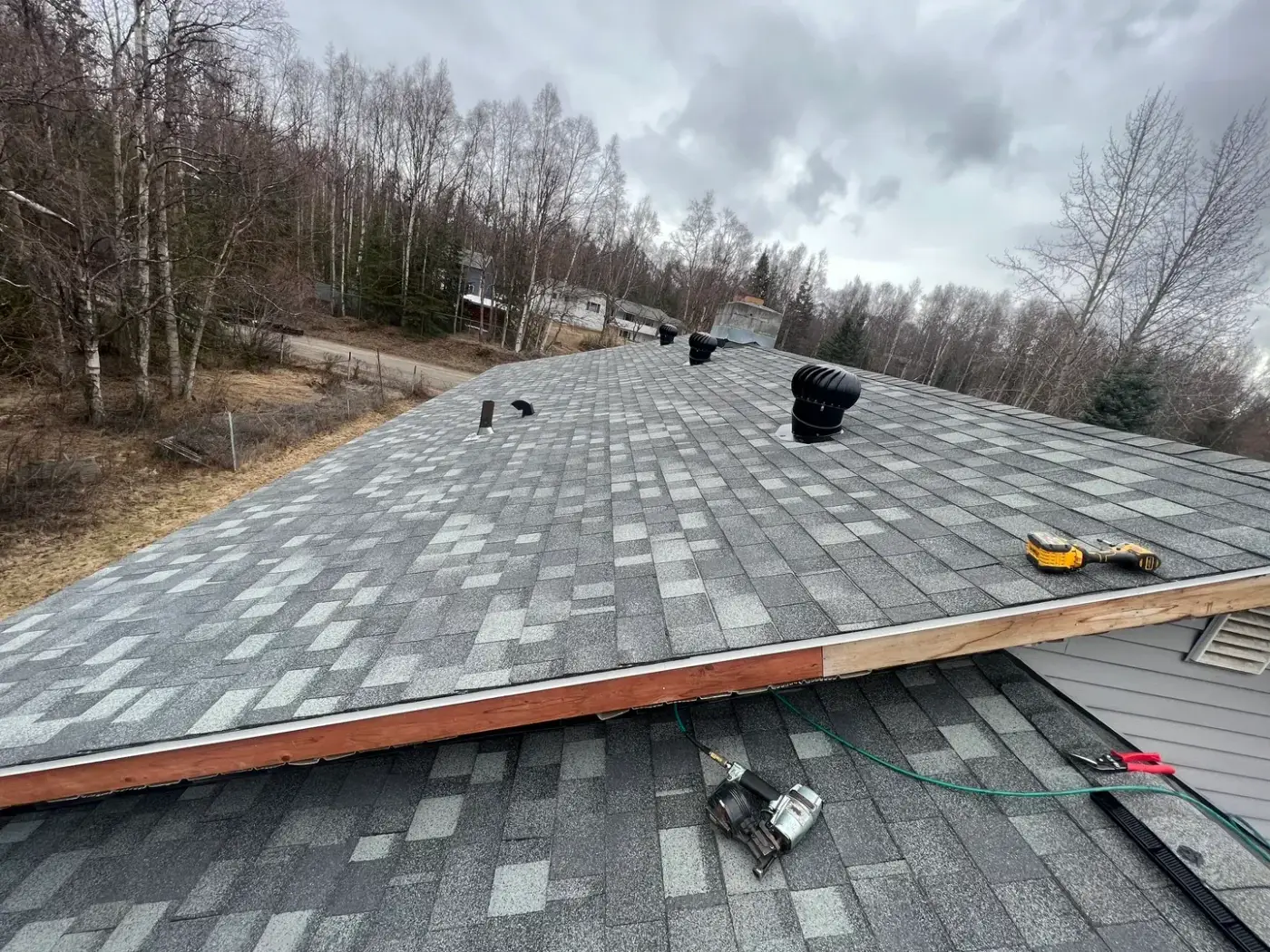 Roofing project Anchorage Alaska - newly installed shingles ventilation pipes and tools on sloped roof reflecting quality workmanship