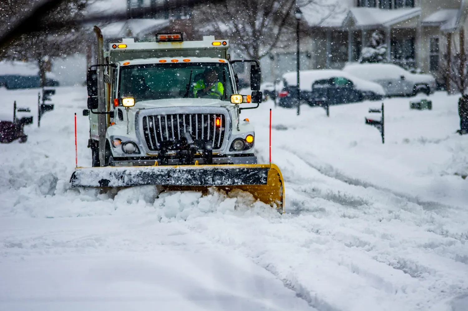Snow plow clearing residential streets in Anchorage, Alaska, during winter snowfall, highlighting snow removal services.